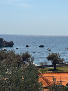 Red clay tennis court is situated along a scenic coastline overlooking the blue sea