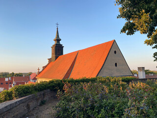 Historic church with a bright orange-tiled roof and baroque bell tower stands in Petrovaradin under a clear blue sky © lmot11
