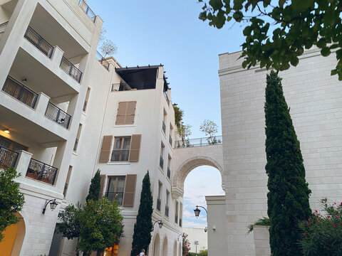 Low-angle view of elegant, white stone residential buildings connected by an arched pedestrian bridge under a clear sky