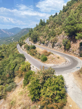 Winding asphalt road curves sharply around a steep, forested mountain slope in a hairpin turn