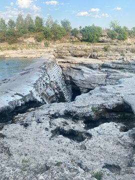 Stone masonry weir stands amid rugged, light-colored rocky terrain beside a calm body of water