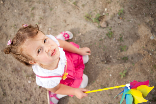 High angle view of a cute little girl holding a colorful pinwheel toy outdoors looking up at camera.