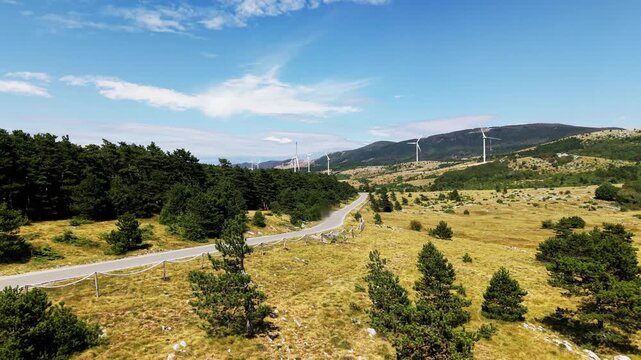 Video showing a mountain plateau covered with grass, scattered rocks and low vegetation, with multiple wind turbines standing along the ridges