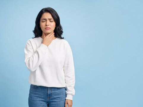 young indian woman with closed eyes touching neck suffering from sore throat and tonsil infection on blue background for medical advertising ad