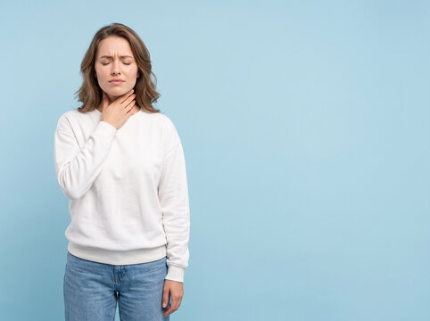 young white woman with closed eyes touching neck suffering from severe sore throat pain on blue background for medical advertising campaign ad