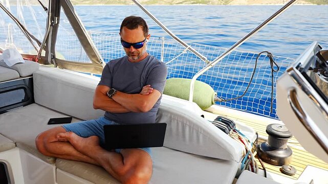 Thoughtful man sitting with laptop on a sailing yacht during a work break. Business planning and location independent lifestyle concept.