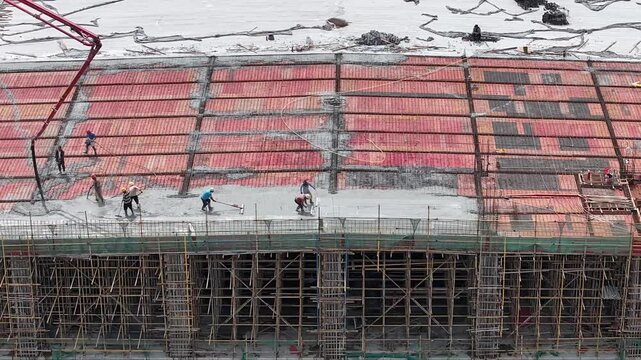 Workers pouring concrete on construction floor with steel rebar and scaffolding