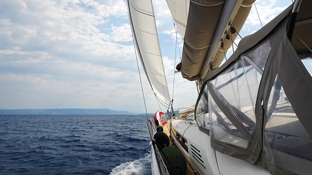 Dynamic view from deck of sailing yacht heeling under wind power while cutting through Adriatic waters. White wake, filled sails, a sense of speed, freedom and offshore adventure