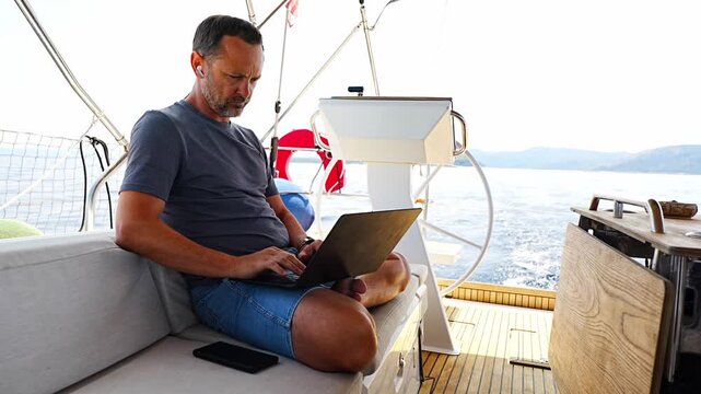 Focused man working on laptop aboard a sailing yacht. Productive remote office in a unique travel environment.