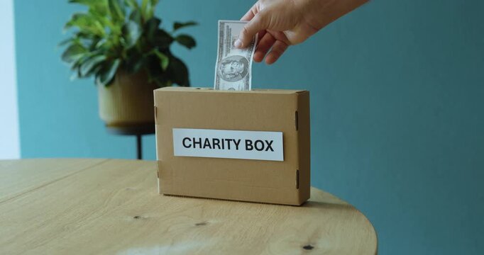Hand donating money into a charity box, representing financial donation, fundraising, generosity and support for people in need.