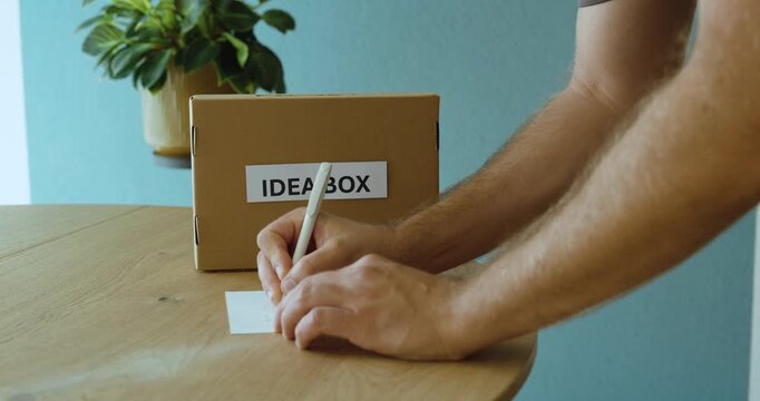 Man writing an idea on a card and submitting it into an idea box, representing employee suggestions, innovation and workplace improvement.