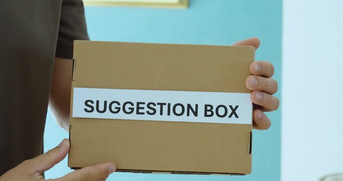 Close-up of a person holding a suggestion box, representing employee feedback, ideas, opinions and workplace participation.