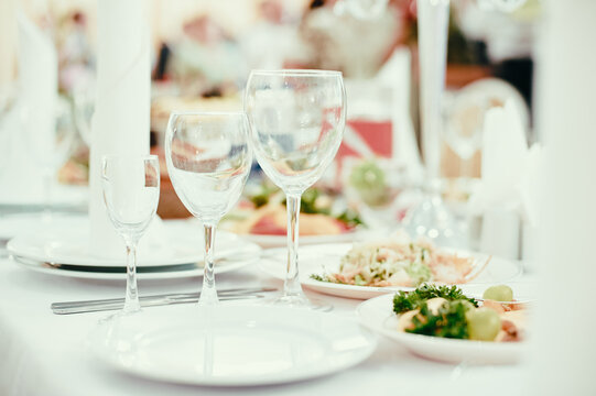 Elegant banquet table with crystal wine glasses, white plates and fresh appetizers arranged for a formal celebration or wedding reception, evoking a festive, romantic and refined dining atmosphere.