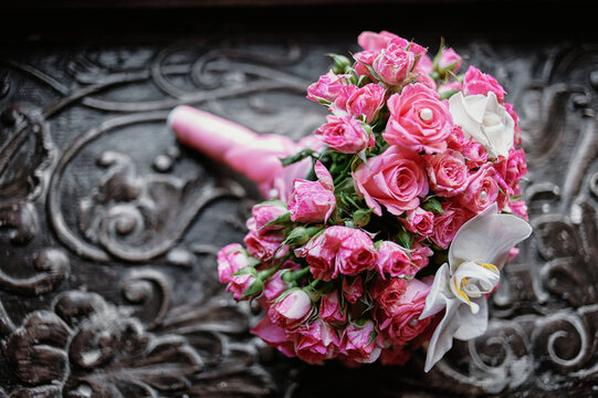 A romantic pink rose bridal bouquet with white orchids rests on ornate dark carved wood, evoking wedding elegance, femininity and vintage charm for invitations, celebrations and floral design.
