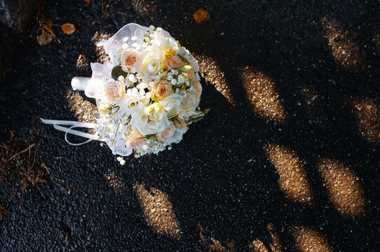 soft pastel wedding bouquet of white and blush roses with baby's breath rests on sunlit asphalt, casting delicate shadows and suggesting romance, quiet celebration, and intimate post-ceremony moments