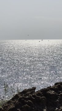 Sparkling sea water shimmers under bright daylight with a rocky shoreline in the foreground