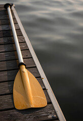 Fototapeta premium Summer vacation and outdoor recreation, yellow kayak paddle resting on a wooden dock by the calm water at sunset for travel and leisure lifestyle