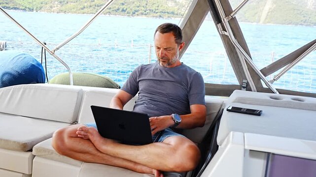 Focused man working on laptop aboard a sailing yacht. Productive remote office in a unique travel environment.