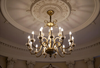 Obraz premium Luxury interior design and opulence, classic gold chandelier hanging from a decorative ceiling medallion in a grand historic building hall