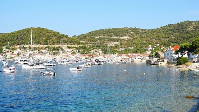 Panoramic view of the harbor with boats, yachts, historic waterfront, stone houses and green hills along the Adriatic coast on a sunny summer day.
