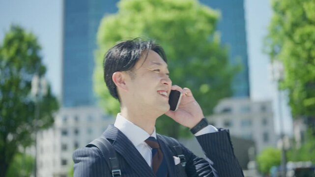 Smiling Japanese businessman on a phone call in a tree lined plaza