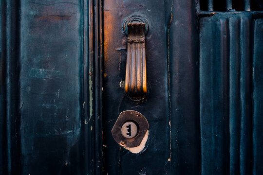 Close up of an antique brass door knocker and keyhole on a weathered dark blue wooden door in Lisbon.