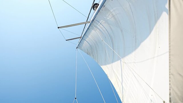 White sails filled with wind against a blue sky above a sailing yacht. Wind powered navigation and freedom at sea.