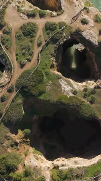 Vertical aerial showcasing the dramatic rock formations and sea grottos at Ponta Jo&atilde;o de Arens on the Algarve coast.
