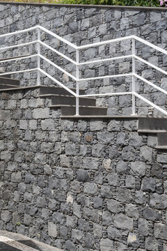 Contemporary outdoor staircase with geometric white railings, dark steps and natural stone cladding used in modern architectural landscaping.
