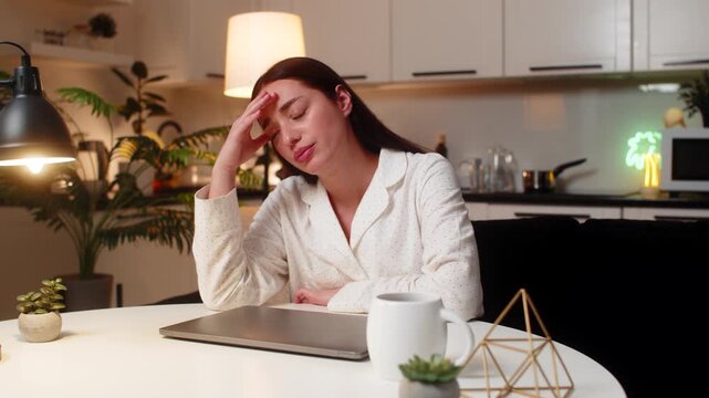 Young woman at night home shuts laptop after work feels burnout wants pause takes breath. Caucasian girl on sofa at table at evening looks tired says enough rubs temples needs break rests eyes closed.
