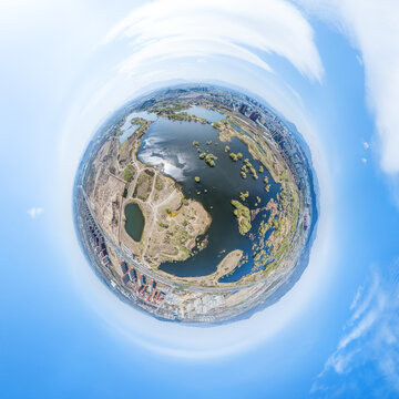 A tiny planet aerial panorama showing a wetland lake with islands, adjacent urban areas under a clear sky.