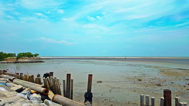 Weathered Wooden Piles Align Along The Shallow Mudflat Edge Under Clear Blue Skies At The Coastal River Estuary In Kuala Selangor, Malaysia. - pan right shot
