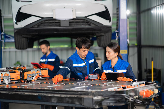 During electric vehicle battery testing, a technician touches a red probe to the pack while a female colleague holds a clipboard.