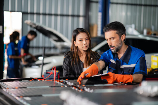 A garage service technician guides a customer through the open battery pack, pointing toward its modules with a pen.