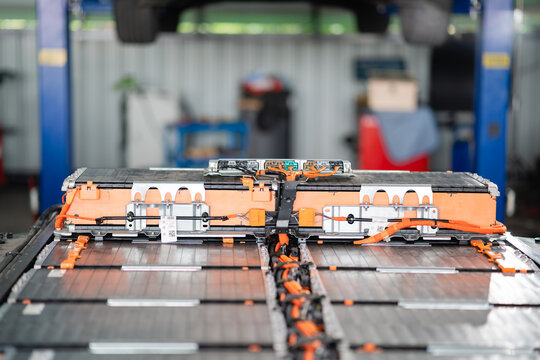 An electric vehicle battery pack sits open on a workshop stand, exposing its junction box, wiring harness and rows of modules.