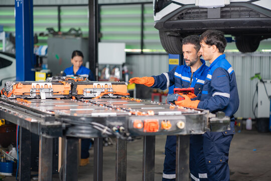 Explaining electric vehicle battery results, a technician gestures over the open pack while a colleague holds a tablet and tester.