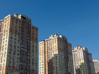 Obraz premium Tall residential apartment buildings stand against a clear blue sky in an urban neighborhood, reflecting modern high-rise architecture and metropolitan living in a sunny city setting
