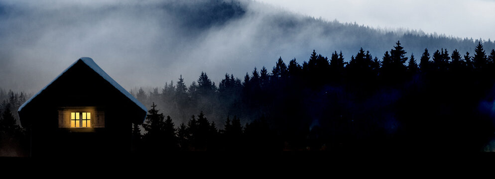 Bergh&uuml;tte mit beleuchtetem Fenster vor dunklem Tannenwald
