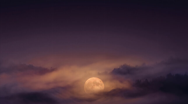 Full moon glowing through thick dense fog in a dark night sky above the horizon with shines through heavy heavy layers rolling