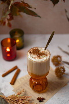 Pumpkin spice latte with whipped cream and gold spoon, cozy autumn drink with candles