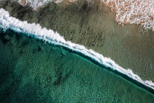An ocean wave breaks along a turquoise coloured, pristine, reef-lined sandy shore. Captured on a beautiful idyllic sunny day from high above the beach on the South Coast of New South Wales, Australia.