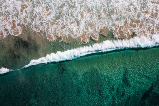 An ocean wave breaks along a turquoise coloured, pristine, reef-lined sandy shore. Captured on a beautiful idyllic sunny day from high above the beach on the South Coast of New South Wales, Australia.