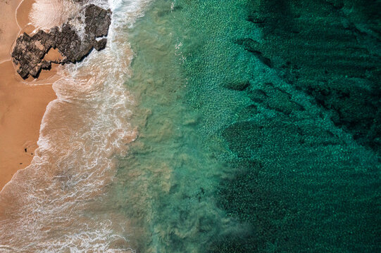 An ocean wave breaks along a turquoise coloured, pristine, reef-lined sandy shore. Captured on a beautiful idyllic sunny day from high above the beach on the South Coast of New South Wales, Australia.