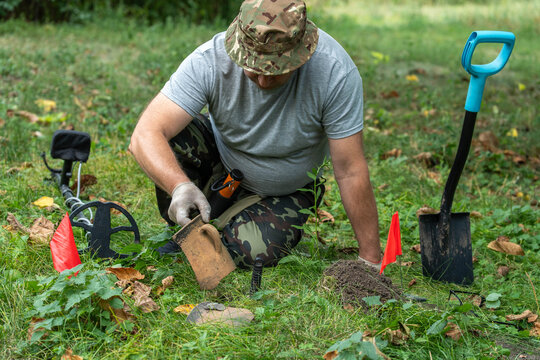 A dedicated treasure hunter carefully digs into the earth, revealing a buried artifact. Colorful flags mark the area as he searches for lost items in a vibrant, green landscape