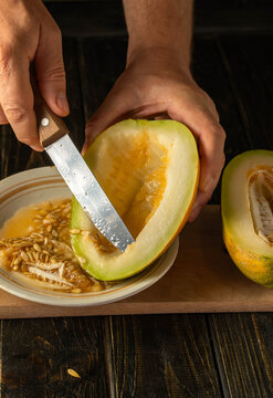 A person's hands skillfully slice open a vibrant melon in a warm kitchen. The fruit's juicy flesh contrasts with its hard exterior, and seeds spill onto a plate below