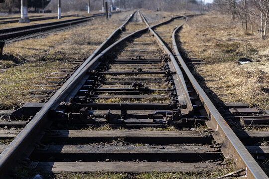 A railway switch mechanism joins metal tracks on a rural path, creating a detailed perspective of steel infrastructure lines that symbolize travel, industrial progress and crossroads