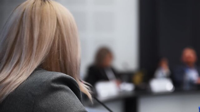 Female speaker talking into a microphone during a professional conference with participants in the background. Public speaking, business event, presentation and corporate communication.