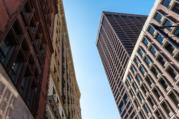 Tall urban skyscrapers loom over narrow street with clear blue sky © Allison