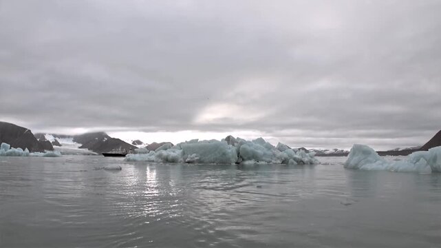 Dense Field of Floating Ice in Cold Coastal Mountain Seascape. The view includes multiple white and pale blue ice floes cover the foreground with low dark mountains beneath gray cloud.