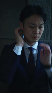 Tired Japanese businessman rubbing his neck in a dim office arcade
